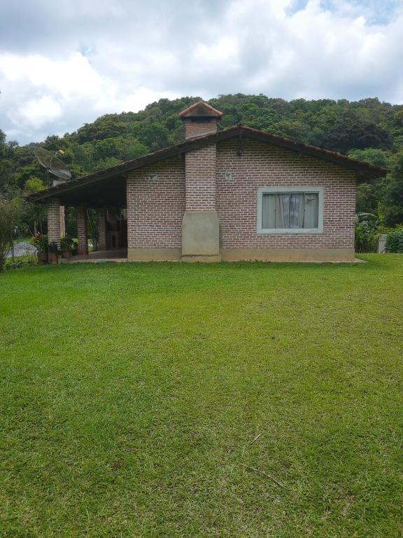 a brick house with a window and a grass yard at Chácara Pousada in Juquitiba