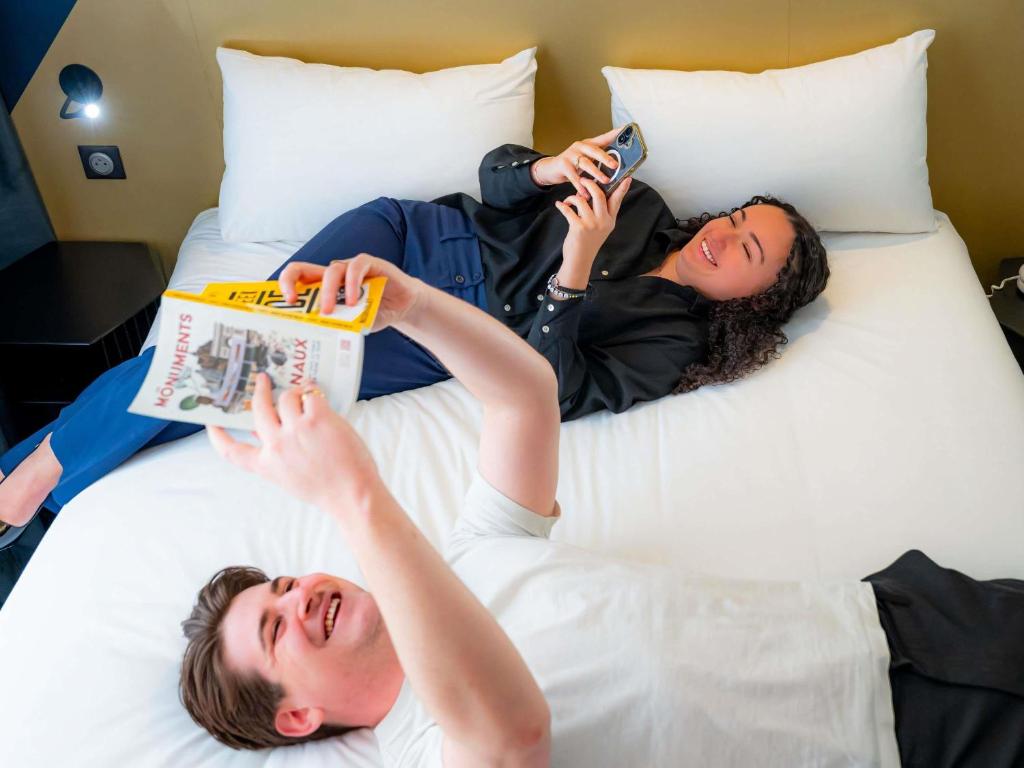 two people laying on a bed while taking pictures at ibis Styles Paris 15 Lecourbe in Paris