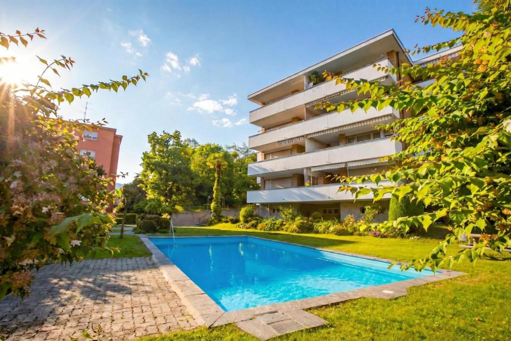an apartment with a swimming pool in front of a building at Malibu46 - Minusio Apt with Shared Pool & Balcony - Happy Rentals in Minusio