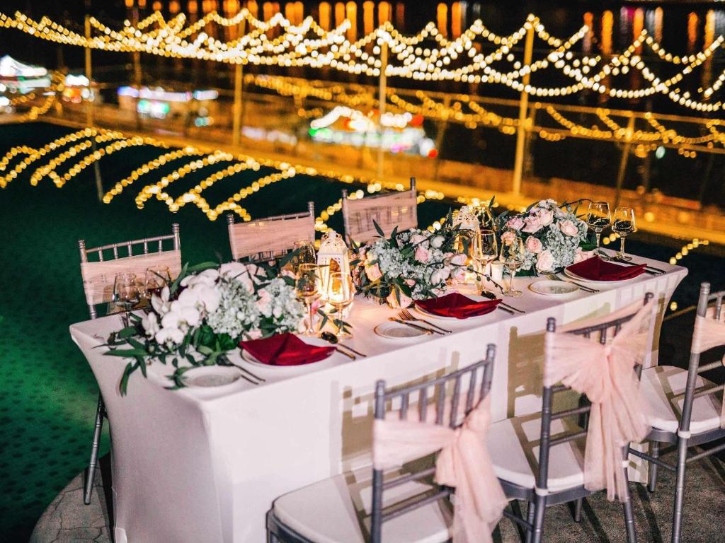 A candlelit banquet table on an elevated terrace, backed by glowing city lights.