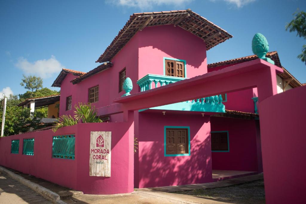a pink house with a sign on it at Morada Coral Hostel em Maracaípe in Porto De Galinhas