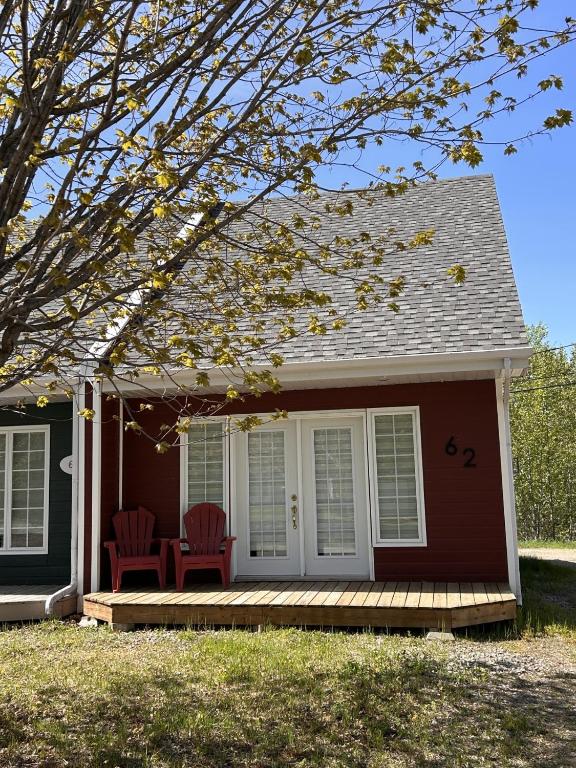 a small house with two red chairs on a porch at La Cachette in LʼAnse-Saint-Jean