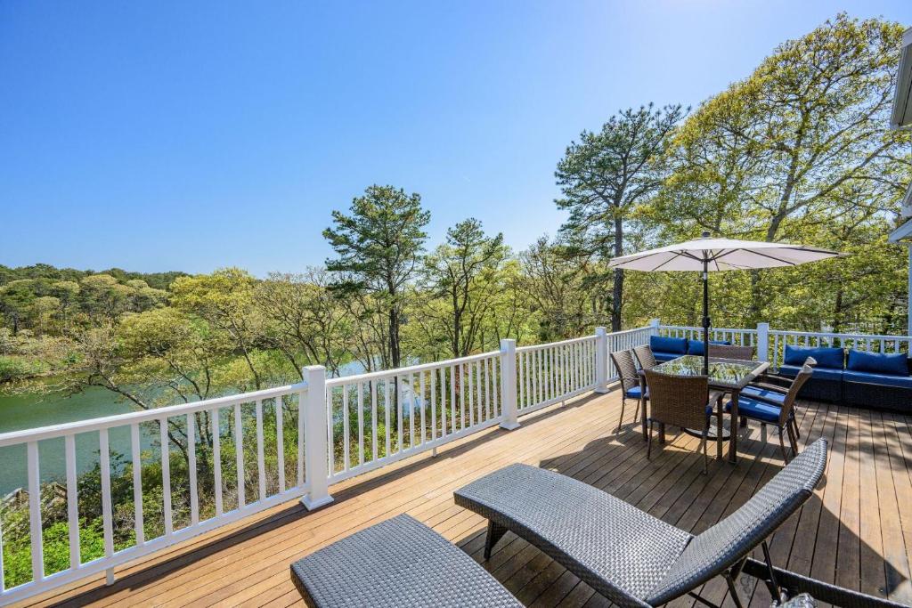 a deck with a table and chairs and an umbrella at Lake front, Near Beach, AC, WiFi, Pet Friendly near Bike Path in Chatham