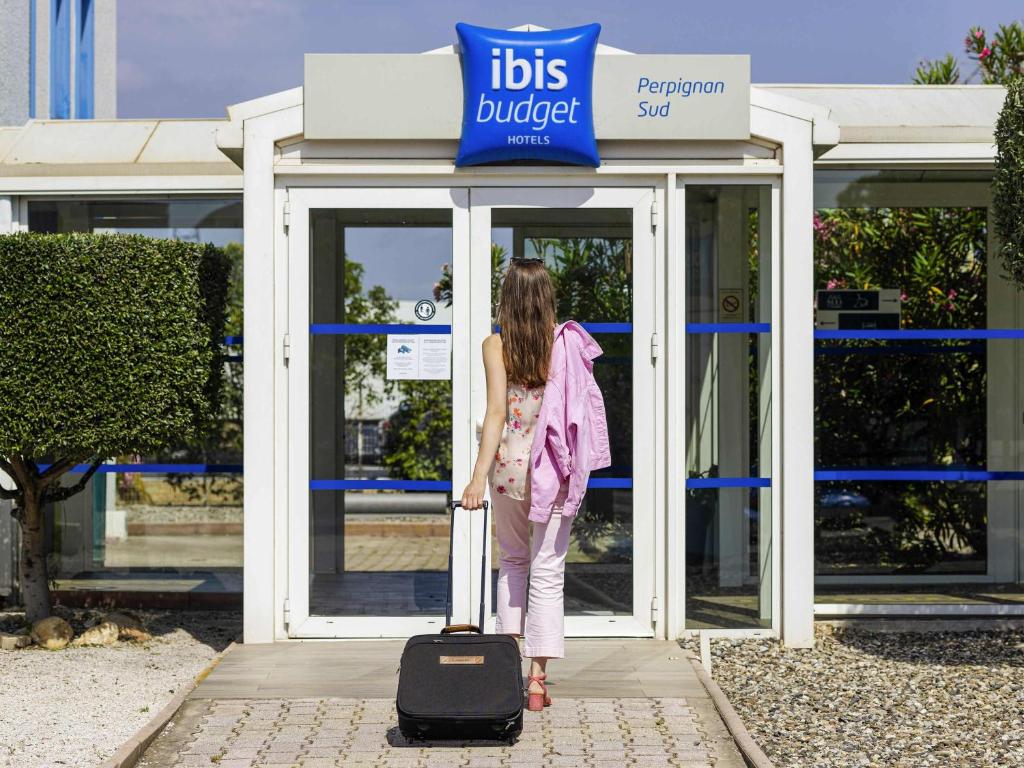 a woman standing in front of a store with a suitcase at Ibis Budget Perpignan Sud in Perpignan