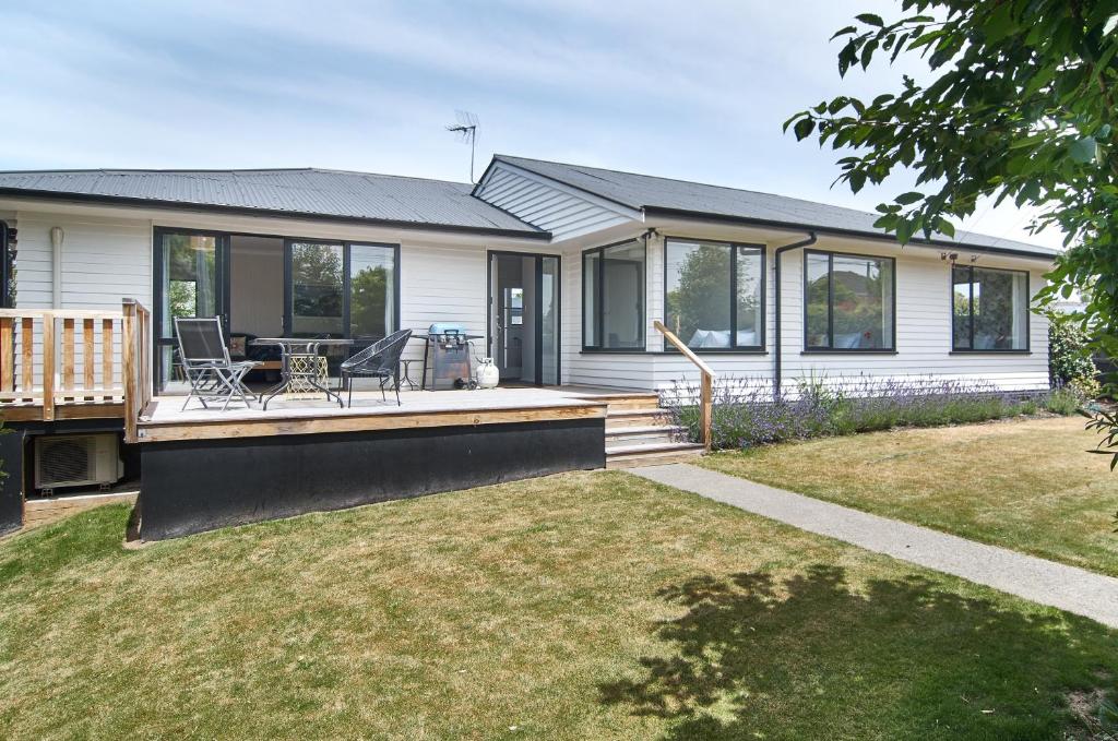 a white house with a deck with a table and chairs at Brookside Villa - Christchurch Holiday Homes in Christchurch