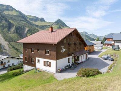 a large building on a hill with mountains in the background at Haus Wilma in Damuls