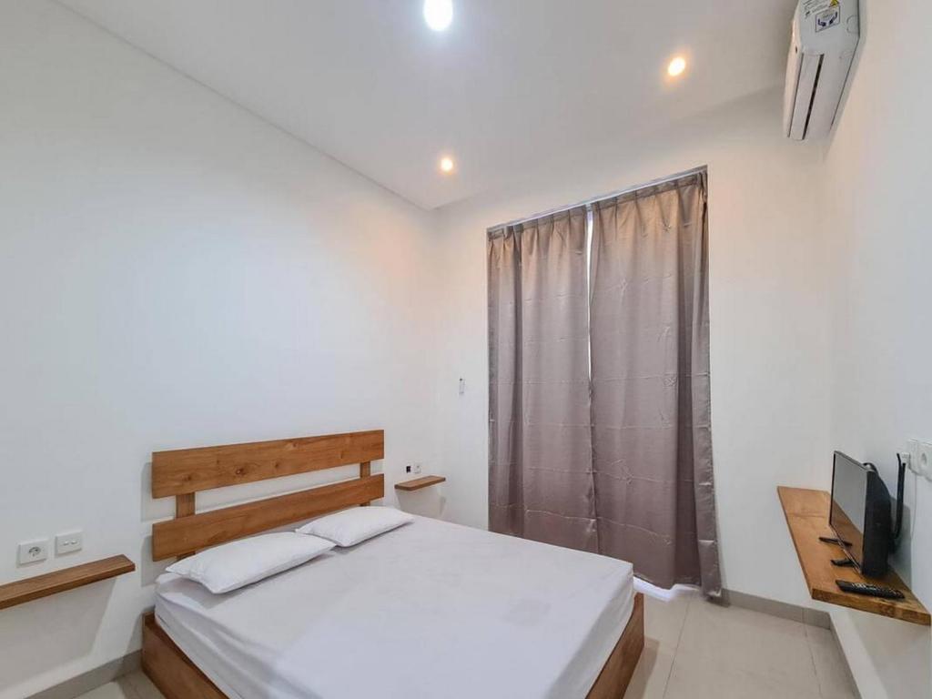 a white bedroom with a bed and a television at Graha Martadinata Syariah Mitra RedDoorz in Tasikmalaya