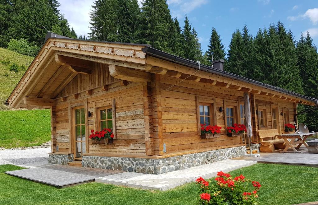 a log cabin with red flowers in a yard at Almhütte Eibingalm in Saalbach-Hinterglemm