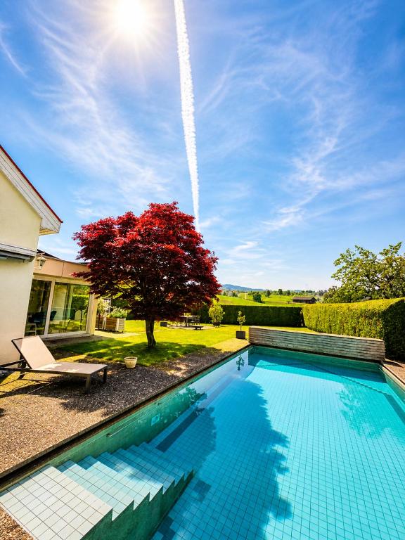 a swimming pool in front of a house with a red tree at Stylish house with garden, sauna & pool in Mörschwil