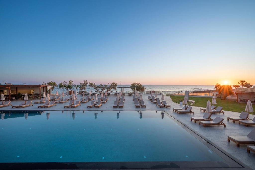 a pool with chairs and the ocean in the background at Oya Beach Resort in Hersonissos