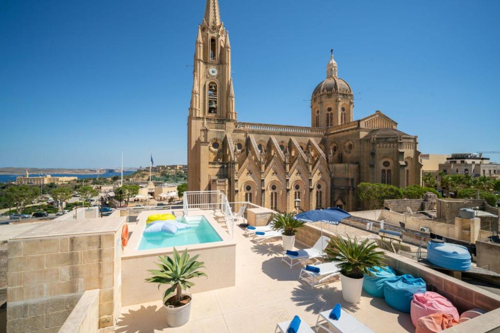 a large building with a clock tower and a swimming pool at The White Knight Premium Boutique Hotel in Għajnsielem