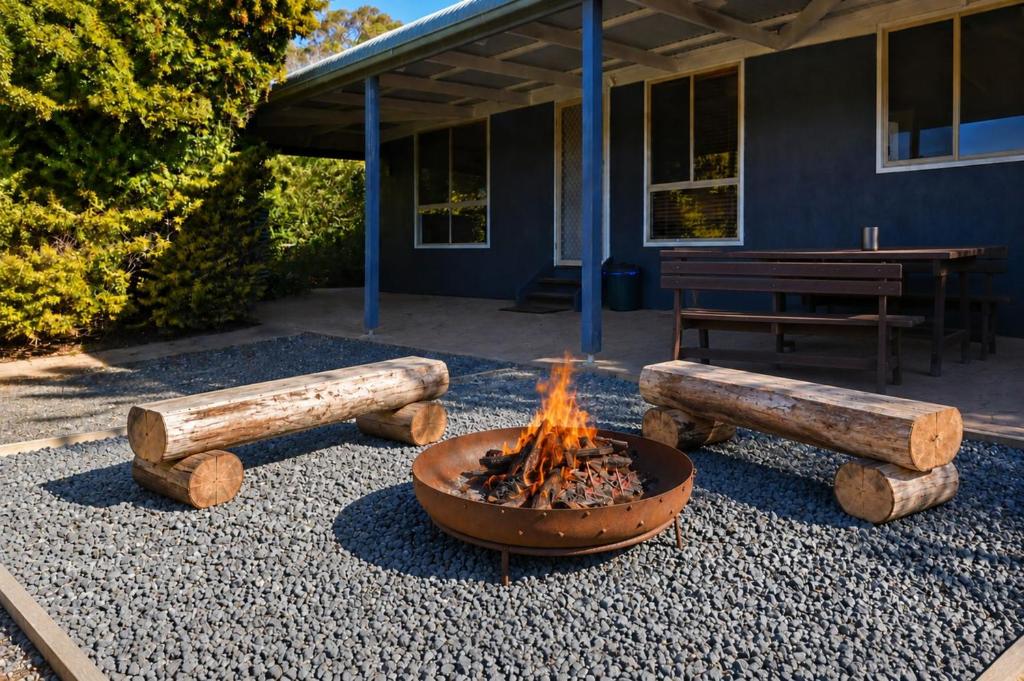 a fire pit with logs around it in front of a building at Palmers Lane Vineyard Cottage in Pokolbin
