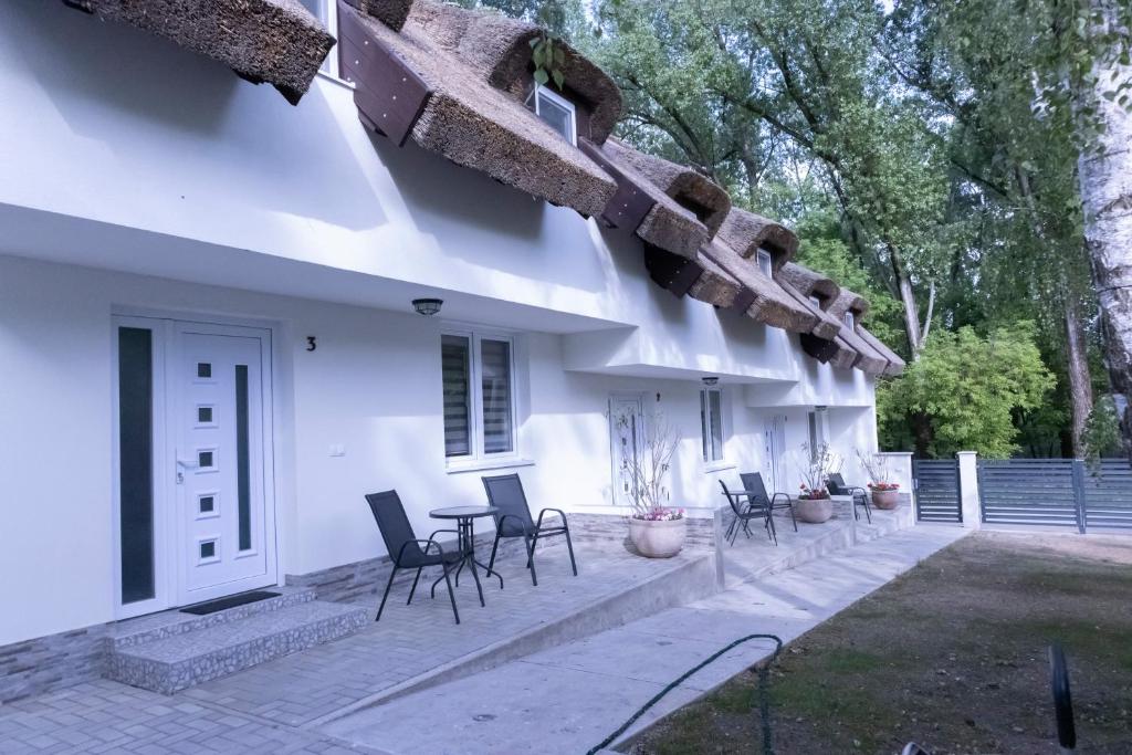 a patio of a white house with chairs and tables at Tisza Apartman Mártély in Mártély