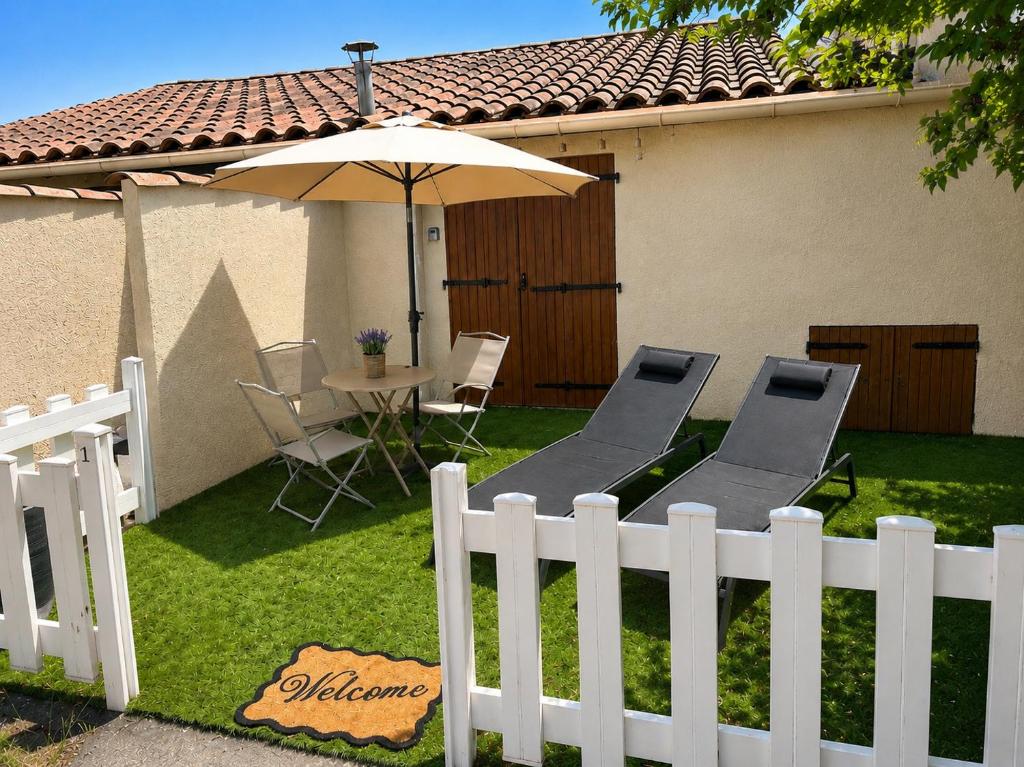 a white fence with chairs and an umbrella in a yard at Maisonnette cosy avec jardinet et parking privatif in Gréoux-les-Bains