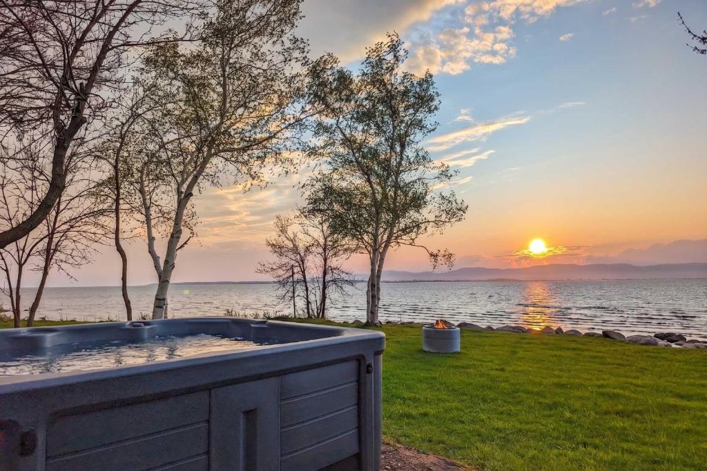 a hot tub in the grass near the water with a sunset at Chalet #2 Waterfront with Spa, Fireplace Wifi & AC in Cap-Saint-Ignace