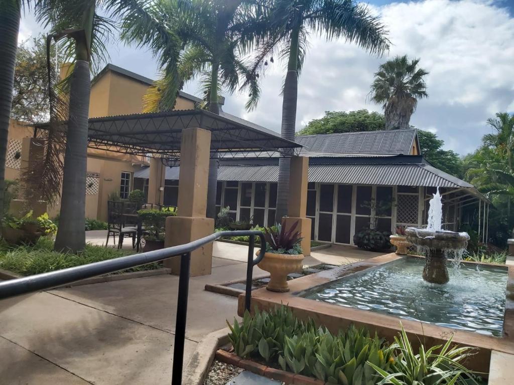 a fountain in front of a building with palm trees at Old Mine Guesthouse in Musina