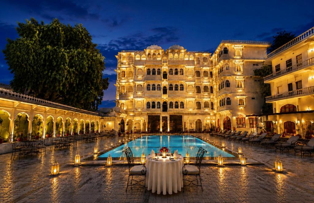 a large building with a table in front of a pool at The Amar Mahal Luxury Heritage Hotel Near Fateh Sagar Lake, Udaipur in Udaipur