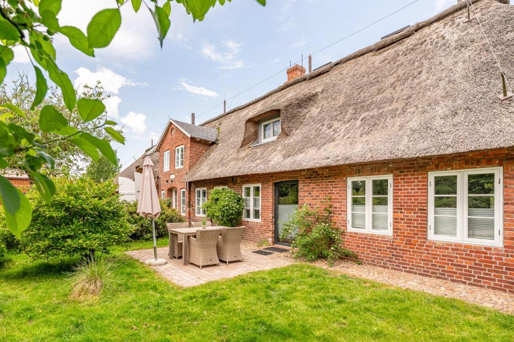 ein Backsteinhaus mit Reetdach und Terrasse in der Unterkunft FeWo Watt-Lounge zwischen Husum und Nordstrand in Wobbenbüll