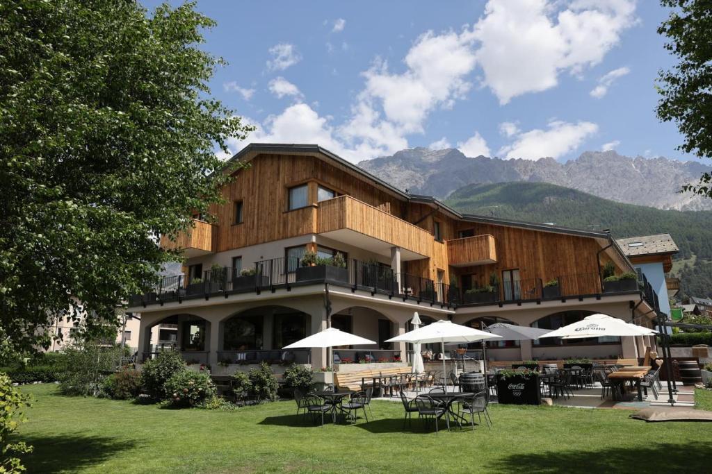 Alpine wooden hotel with balcony rooms, outdoor terrace with white umbrellas and Coca-Cola sign, lawn and mountain views at Hotel Nevada in Bormio