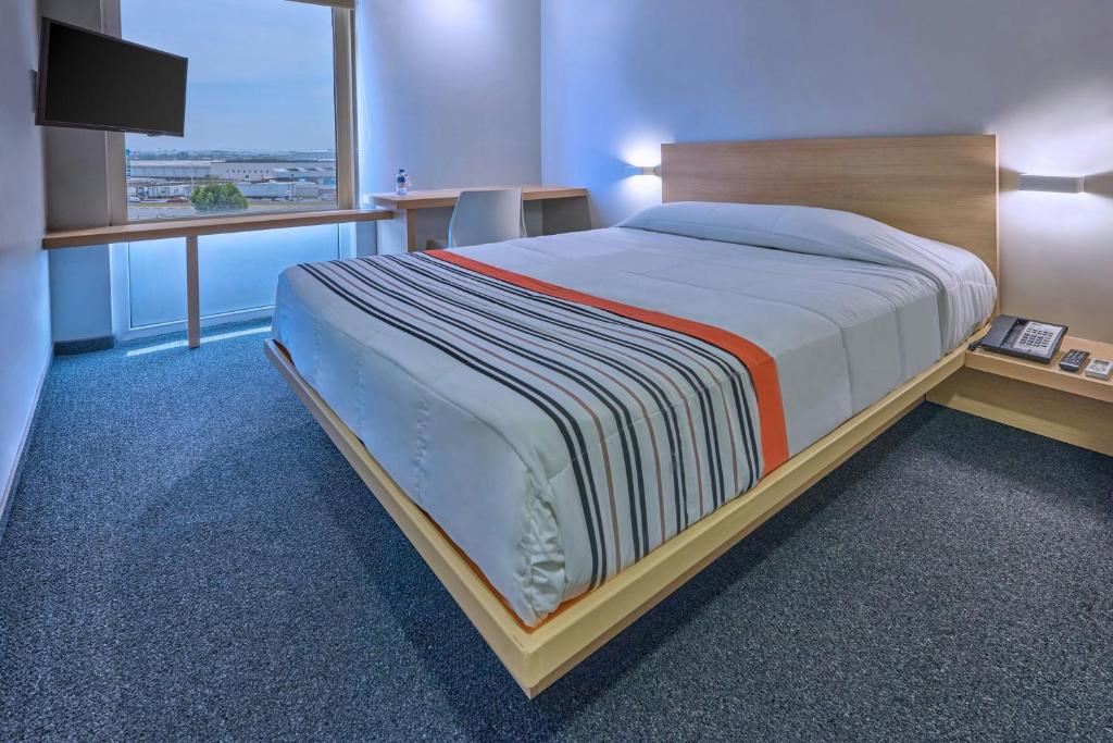 a bedroom with a bed and a desk and a window at City Express Junior by Marriott Guadalajara Periferico Sur in Guadalajara
