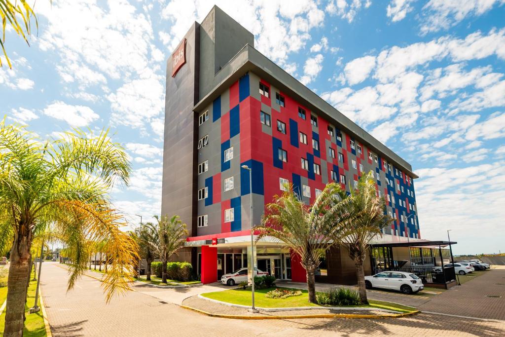 a red and blue building with palm trees in front at Ibis Porto Alegre Assis Brasil - Estacionamento Gratuito para hospedes in Porto Alegre