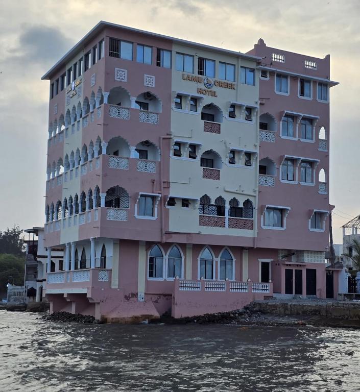 a pink building on the water next to a river at Lamu Creek Hotel in Lamu