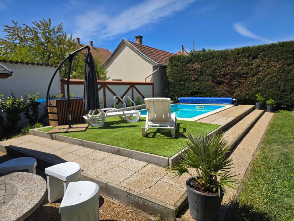 a backyard with a swimming pool with chairs and an umbrella at Martina apartman in Gyula