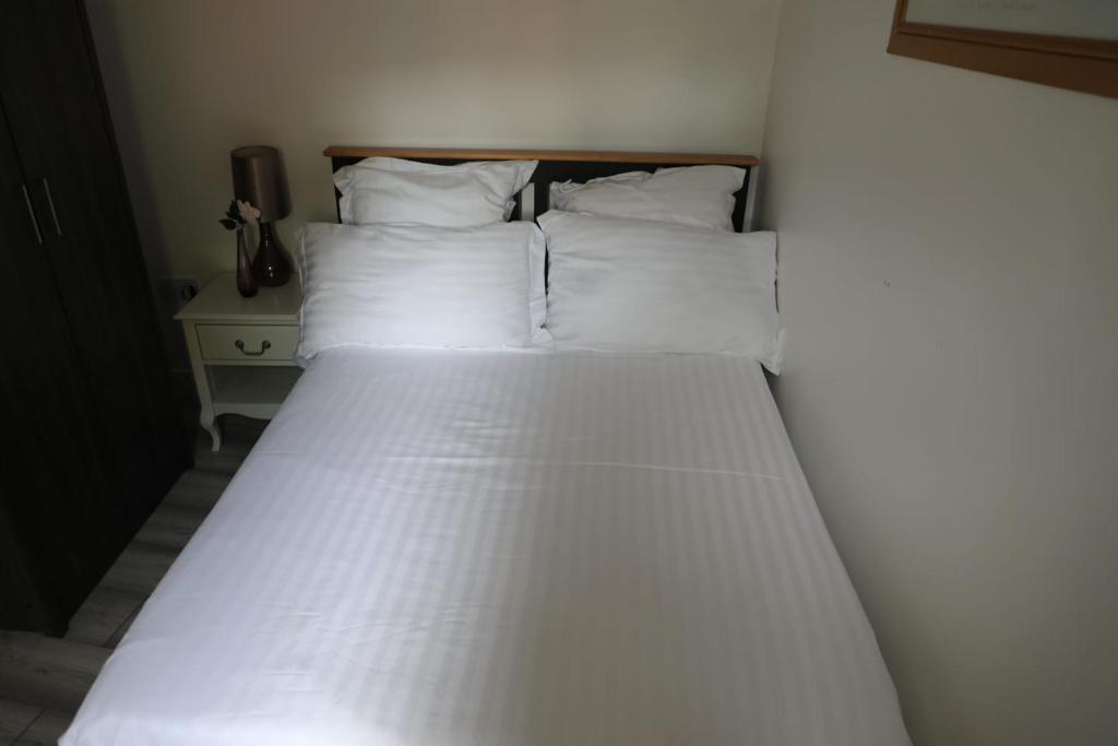 a bed with white sheets and pillows in a room at Comfy Guest suite in Dartford