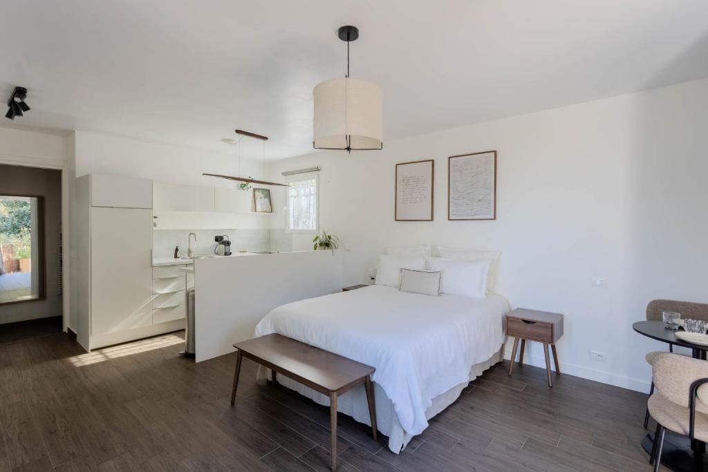 a white bedroom with a white bed and a kitchen at Studio lumineux avec jardin privé et parking in La Turbie