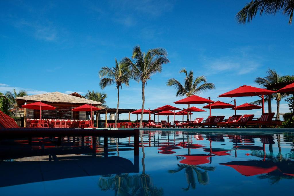 a pool with red umbrellas and chairs and palm trees at Hotel Manati in Barra Grande