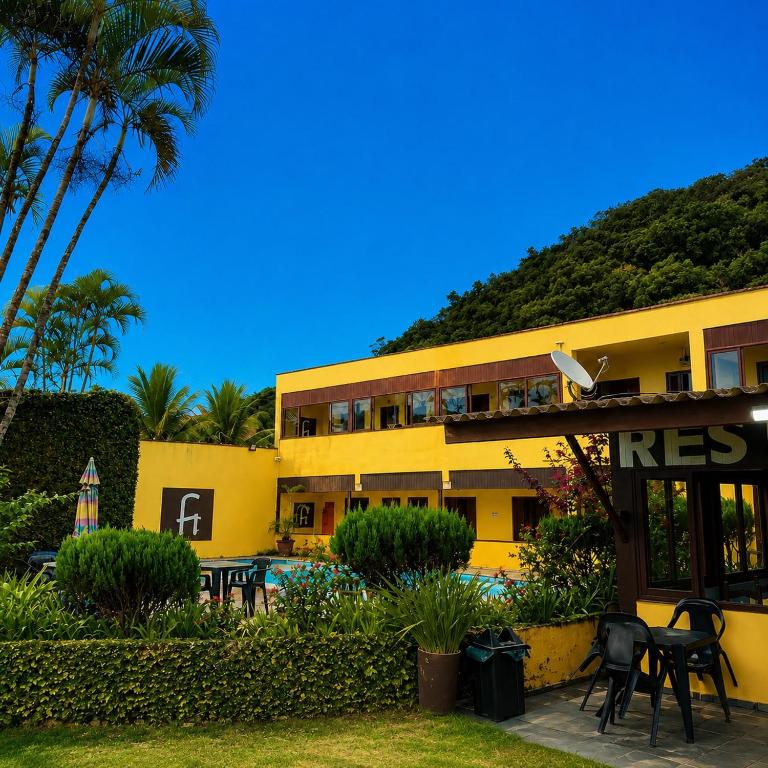 a yellow building with tables and chairs in front of it at Pousada Cantinho do Mar - pé na areia in Guarujá