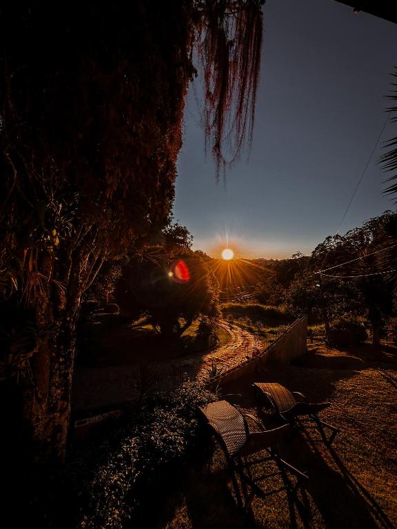 a sun setting over a dirt road with a tree at Pousada Alto do Vale in Nova Friburgo