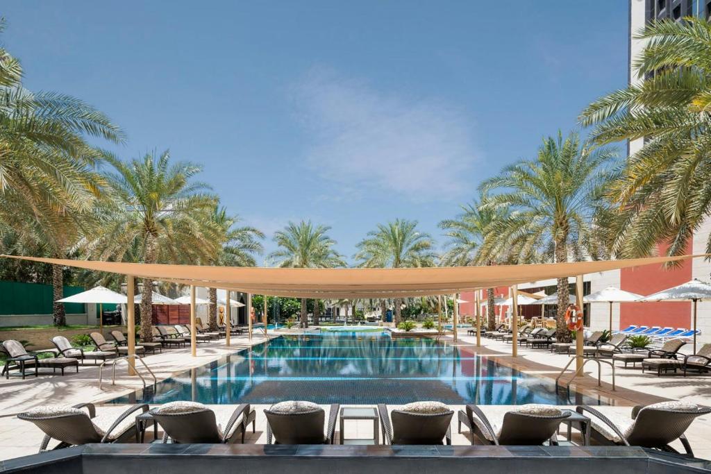 a pool at a hotel with chairs and umbrellas at Sheraton Oman Hotel, Muscat in Muscat