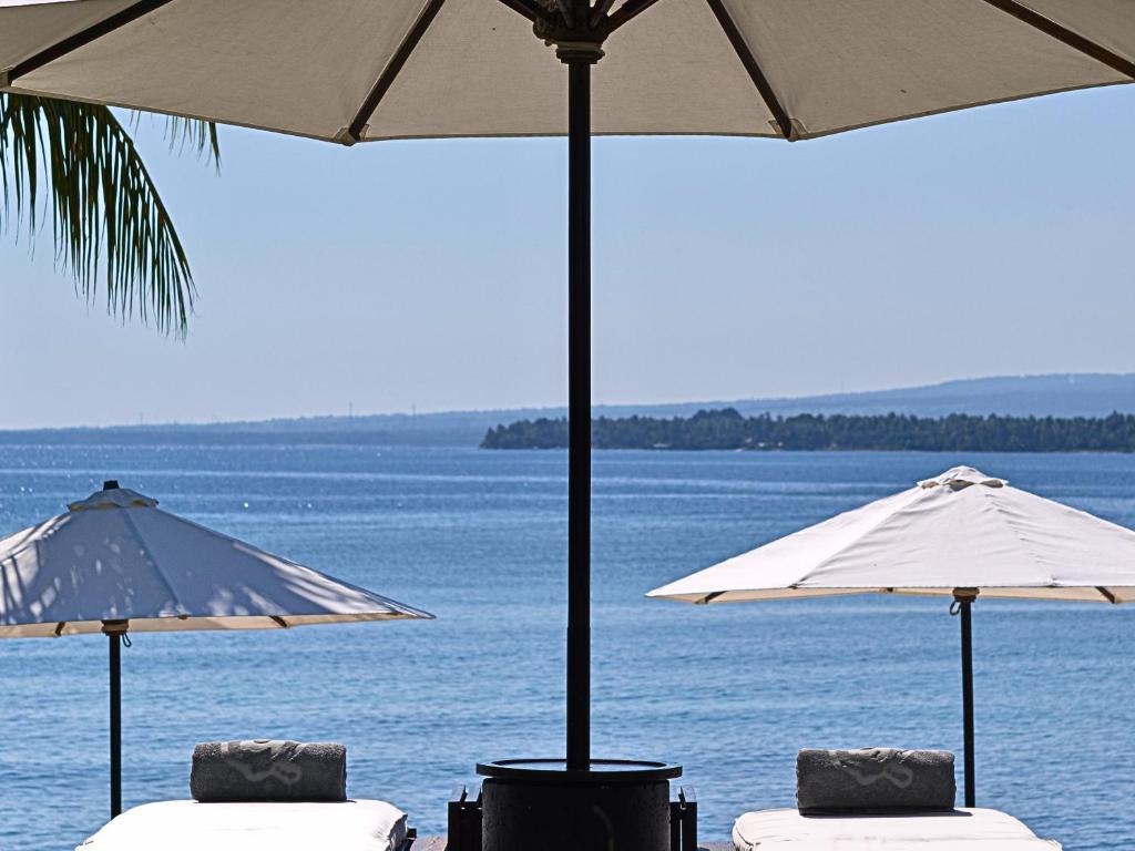 two tables and umbrellas on a beach near the water at 5-Star Boutique Hotel The Lombok Lodge in Tanjung