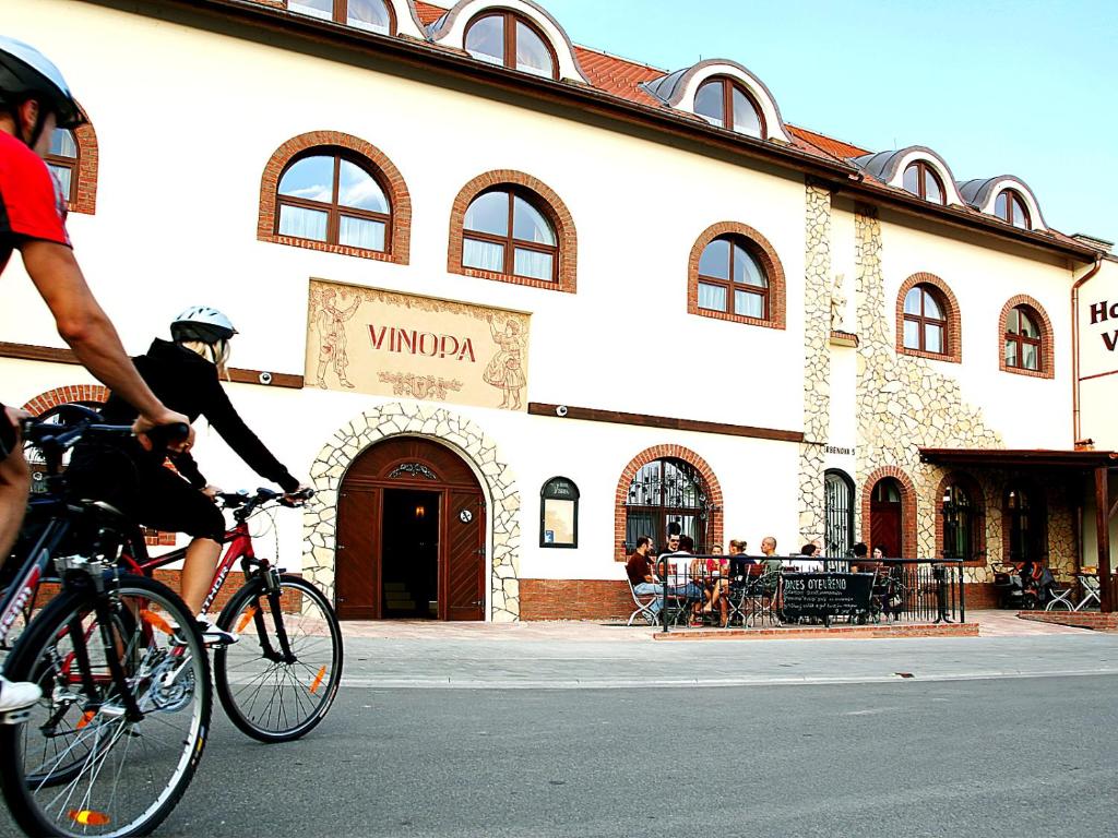 two people riding bikes in front of a building at Hotel Vinopa in Hustopeče