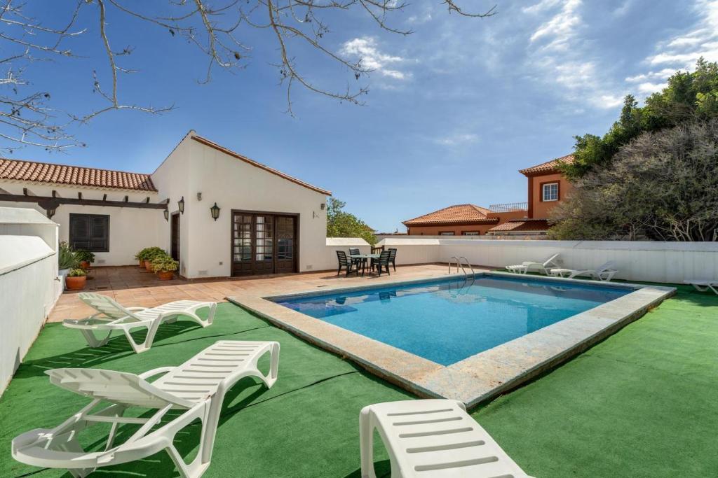 a swimming pool with lawn chairs and a house at Exclusively located Golf Villa with heated pool in San Miguel de Abona