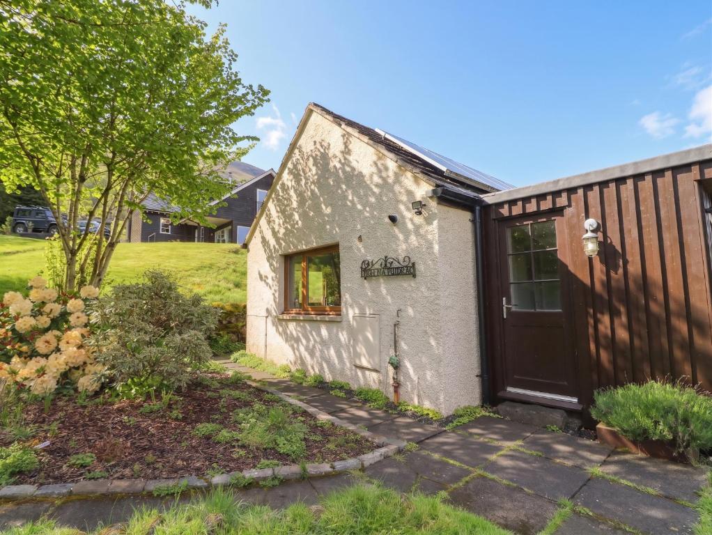 a white building with a door and a yard at Puidrac Cottage in Lochearnhead