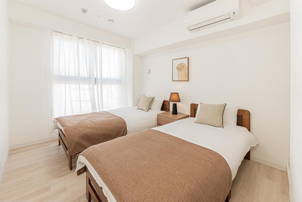 two beds in a white room with a window at 直达池袋丨东京丨银座无需换乘丨地铁站步行3分钟 丨商店街旁 生活出行方便 in Tokyo