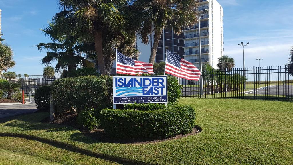Ein Schild in einem Park mit zwei amerikanischen Flaggen in der Unterkunft Islander East Condominiums in Galveston