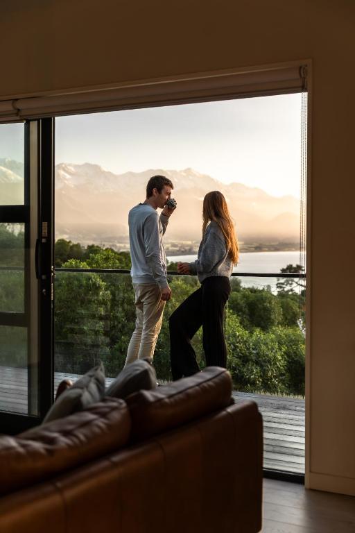 a man and a woman standing in front of a window at Sleek, Elevated Views, Hidden - KK43103 in Kaikoura