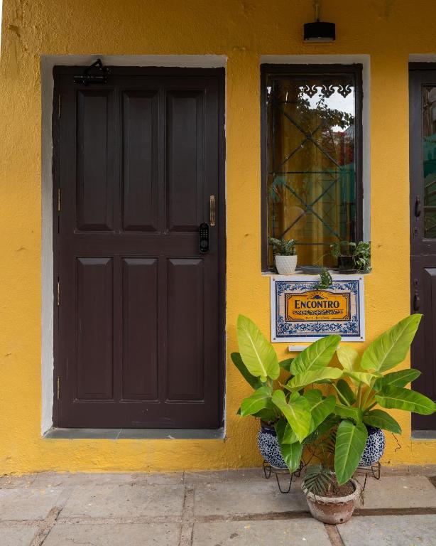 a yellow house with a black door and plants in front at Encontro Homestays in Dona Paula