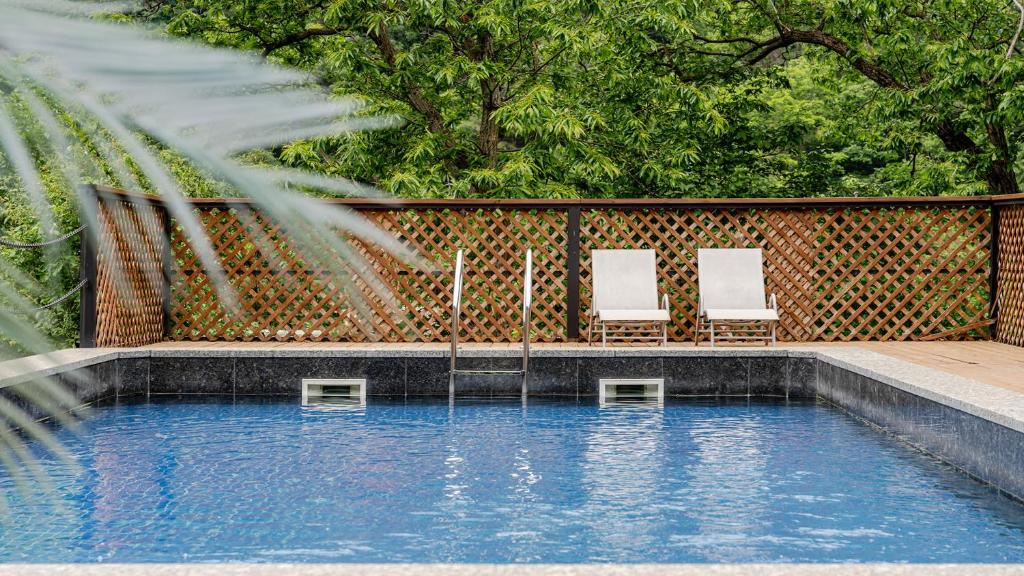 a swimming pool with two white chairs and trees at Gapyeong The Hill Pool Villa in Gapyeong