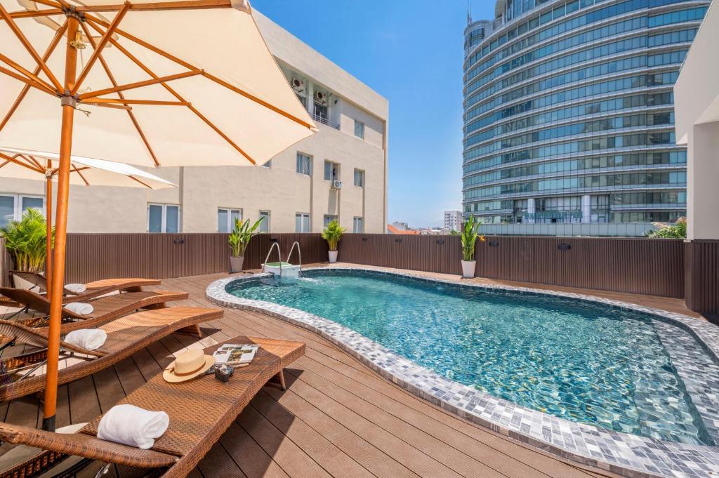 an outdoor swimming pool with tables and chairs and an umbrella at Petro Hotel Da Nang in Danang