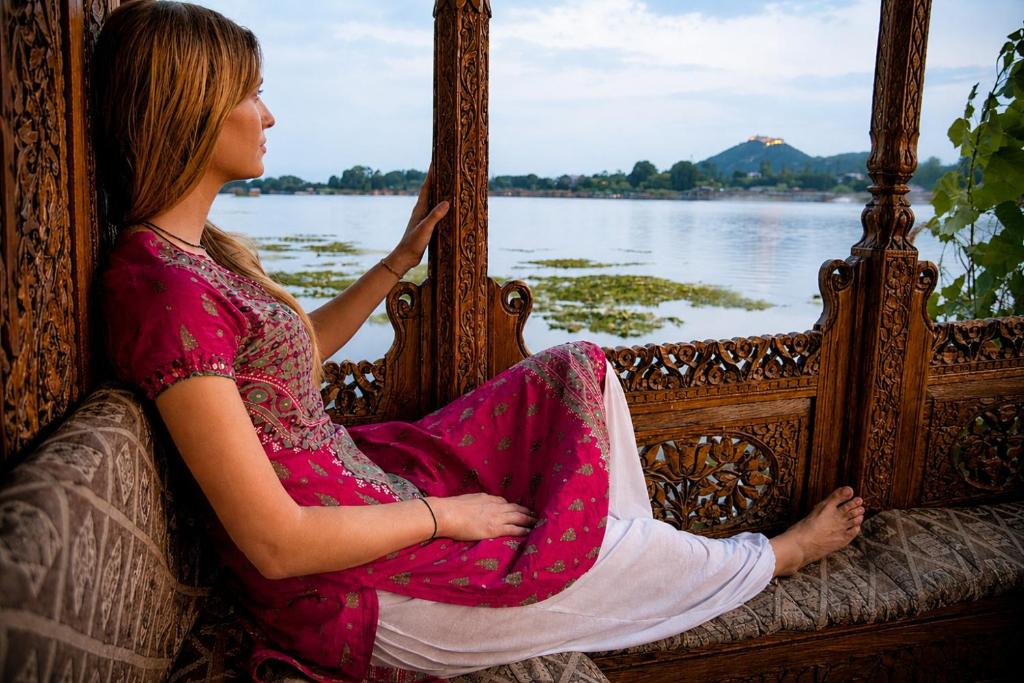 a woman sitting on a bed looking at the water at Heritage Amina Group Of Houseboats in Srinagar