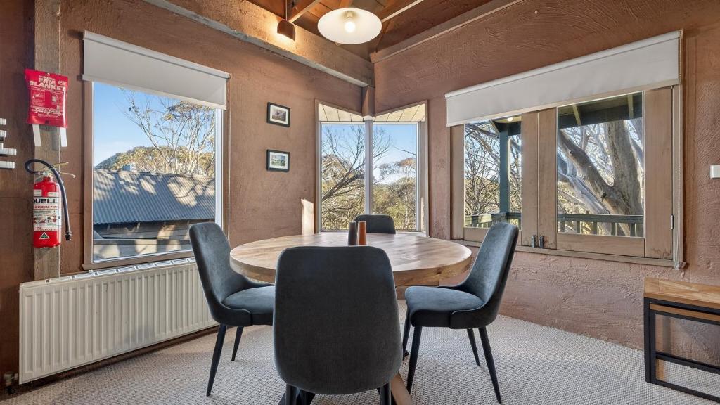 a dining room with a table and chairs and windows at Snowgums 10 in Dinner Plain