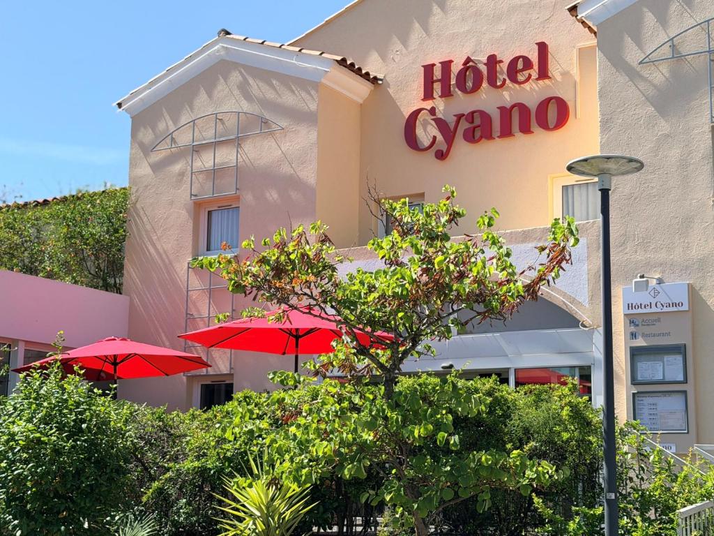 a hotel gamma with red umbrellas in front of it at Hôtel Cyano Fréjus-Saint Raphaël in Fréjus