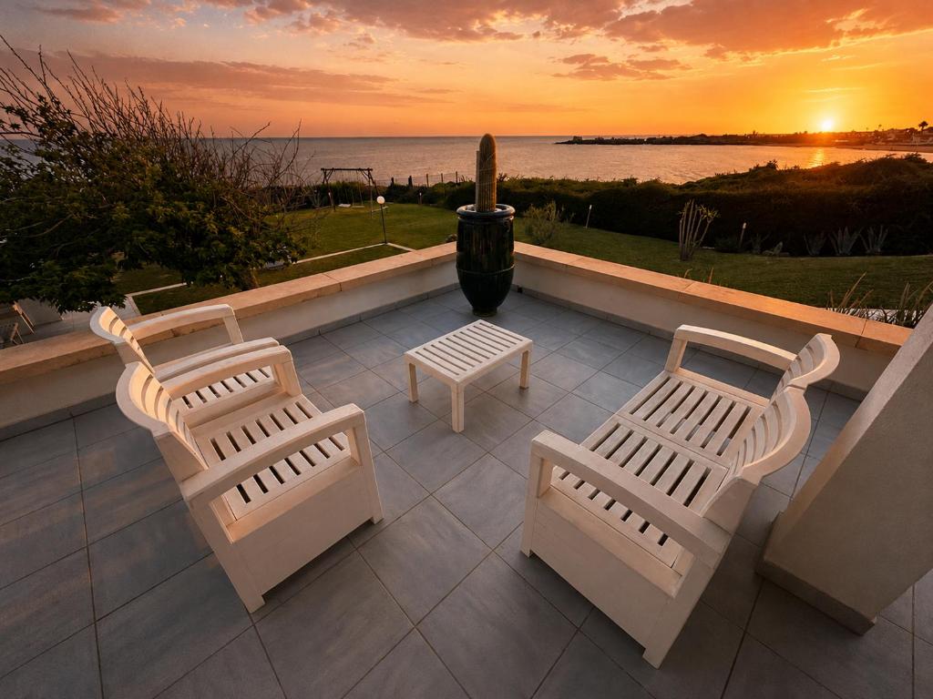 three white benches sitting on a patio with a sunset at Puntabraccetto Sunset in Santa Croce Camerina
