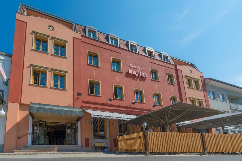 un gran edificio rojo con una sombrilla delante de él en Hotel Raffel en Jennersdorf