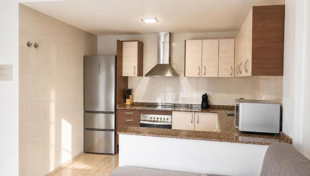 a kitchen with wooden cabinets and a stainless steel refrigerator at Casa 3 hab, piscina, playa, parking, L'Ampolla in L'Ampolla