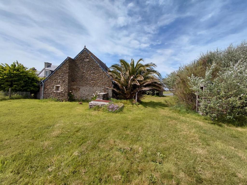 an old stone house in a field with a palm tree at Penty vue sur mer in Tréguennec